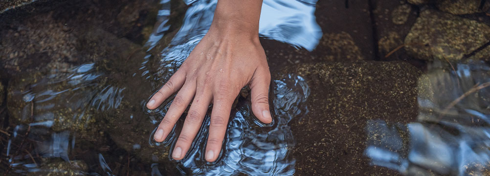 Hand berührt Wasser in einem Bach – Symbol für Gesundheit, Balance und Resilienz